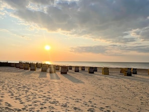 Ein Strand mit blauem Himmel im Sonnenlicht, Fußabdrücken und Liegestühlen.