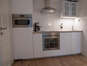 Una cocina con gabinetes blancos, electrodomésticos de acero inoxidable, una cafetera y una planta en maceta.