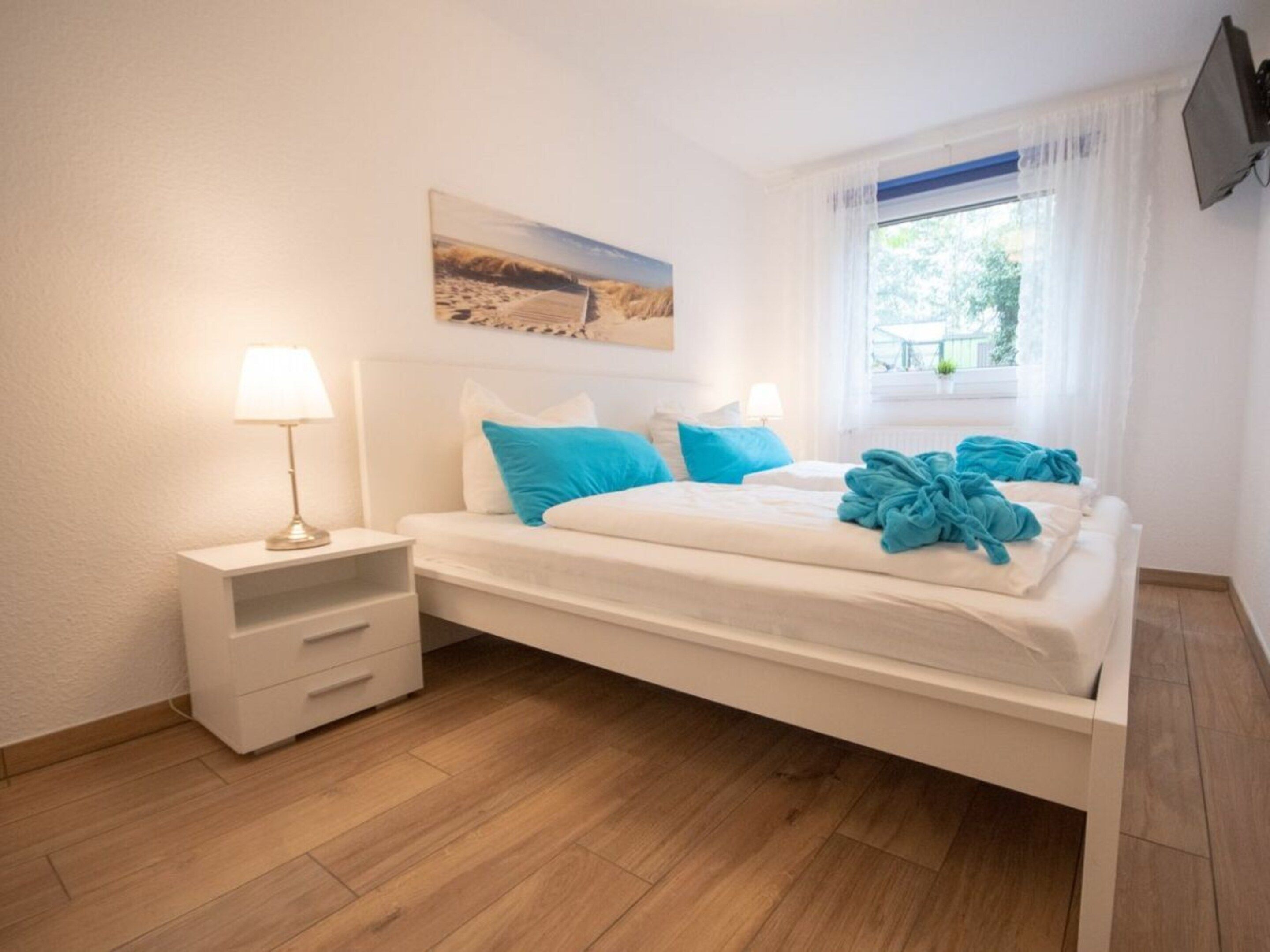 Une chambre à coucher avec un lit, des tables de chevet, une télévision et une fenêtre avec des rideaux.