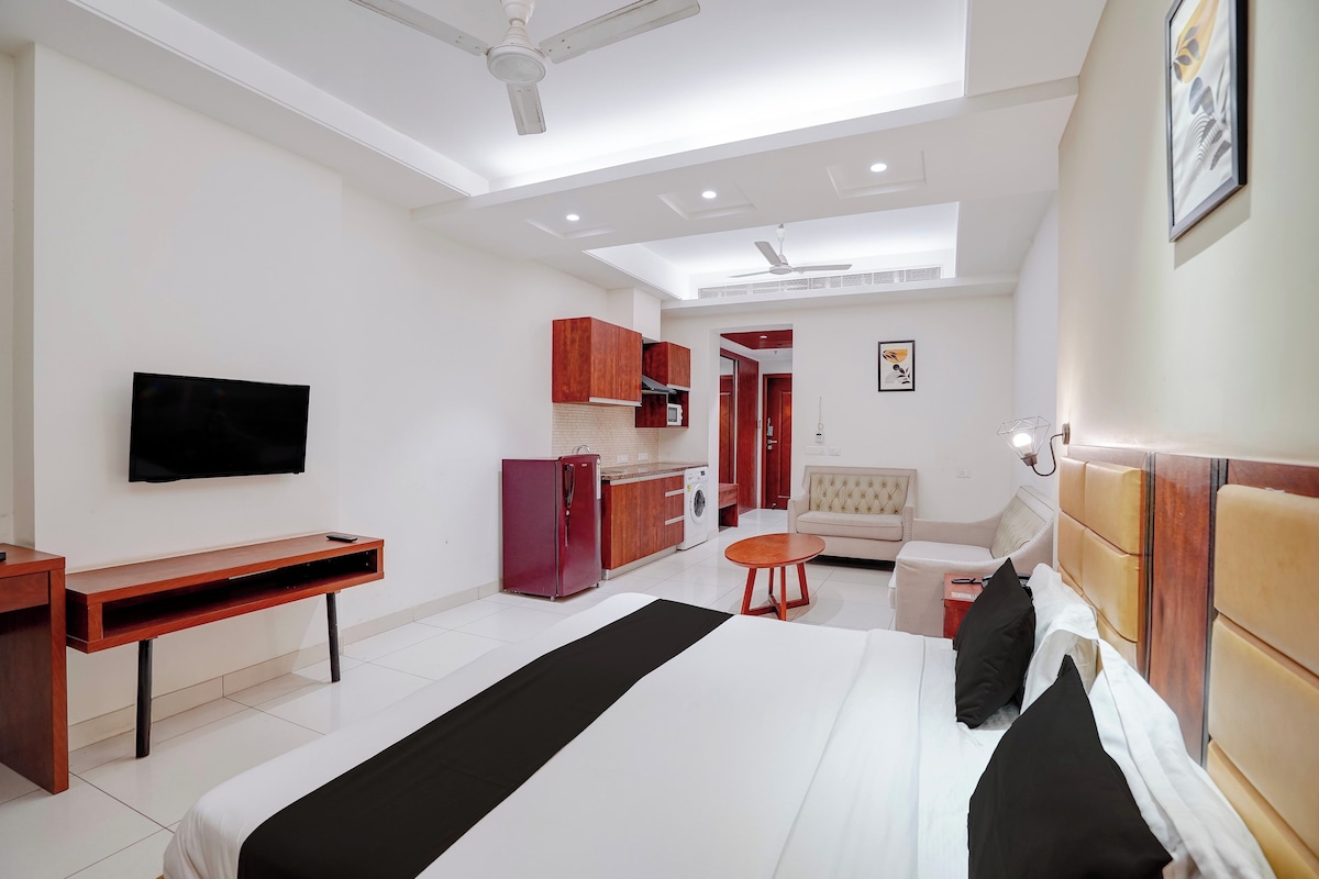 Habitación de hotel con cama, televisión, escritorio, armario, sofá y kitchenette.