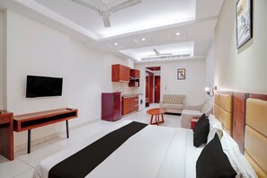Habitación de hotel con cama, televisión, escritorio, armario, sofá y kitchenette.
