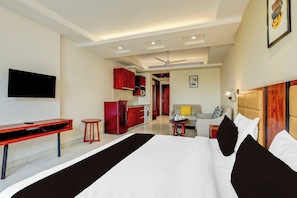 Habitación de hotel con cama, escritorio, silla, televisor, kitchenette y sofá.