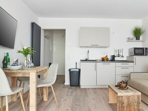 A modern kitchen with white cabinets, a microwave, and a dining area with a wooden table and chairs. - Holiday Apartment 605 (Winterberg)