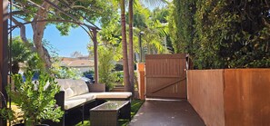 A covered outdoor seating area with a sofa and table, surrounded by greenery and a wooden gate. - La Casita: A Mediterranean Oasis Nestled in the Heart of Santa Monica (Santa Monica)