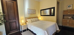 A neatly arranged bedroom with a large bed, bedside lamps, a decorative wall piece, a mirror, and a wooden cabinet.