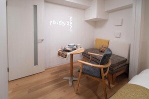 Ein kleiner Raum mit Holzboden, einem runden Tisch mit Stuhl, einer Couch und einem Bett.