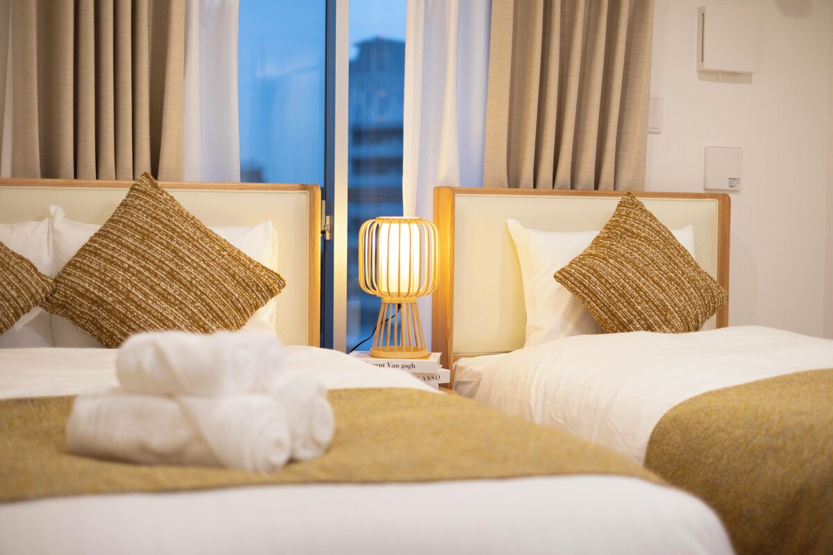 Ein Hotelzimmer mit zwei Betten, jeweils mit Kopfstütze und Kissen. Auf dem Nachttisch zwischen den Betten steht eine Lampe.