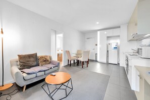 A modern living room with a sofa, coffee table, and a dining area with chairs. - High-rise 1-bed Apartment Near Southern Cross (Melbourne)