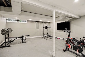 Un gimnasio con una bicicleta estática, banco de pesas y diversos equipos de ejercicio.