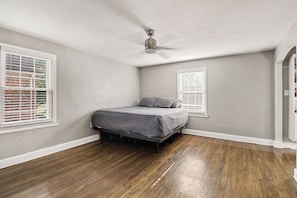 Un dormitorio con cama, ventilador de techo y dos ventanas con persianas.