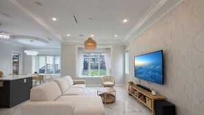 Una sala de estar moderna con un sofá grande, una televisión y un comedor con una araña.