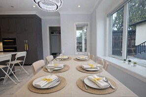 Un espace de repas moderne avec une table dressée pour quatre personnes, une cuisine en arrière-plan et une grande fenêtre offrant une belle vue.