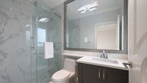 Un baño moderno con cabina de ducha de vidrio, inodoro blanco, tocador con espejo y lavabo.
