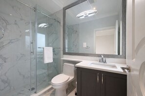 Une salle de bain moderne avec une douche à parois de verre, des toilettes blanches, un meuble-lavabo avec un miroir et un évier.