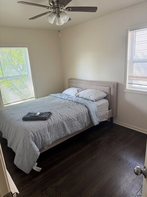 Une chambre à coucher avec un lit, un ventilateur de plafond et une fenêtre avec des stores.