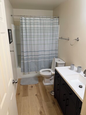Une salle de bain avec un rideau de douche, des toilettes, un lavabo et des placards.
