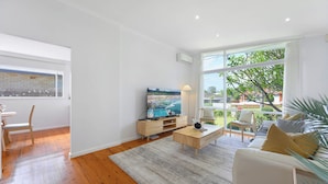 A modern living room with a large window, a flat-screen TV, a coffee table, and a sofa. - 4BR Marsfield Stay  Walk to Macquarie Uni Metro (Marsfield)