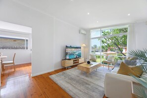 Een moderne woonkamer met een groot raam, een flatscreen televisie, een salontafel en een bank.