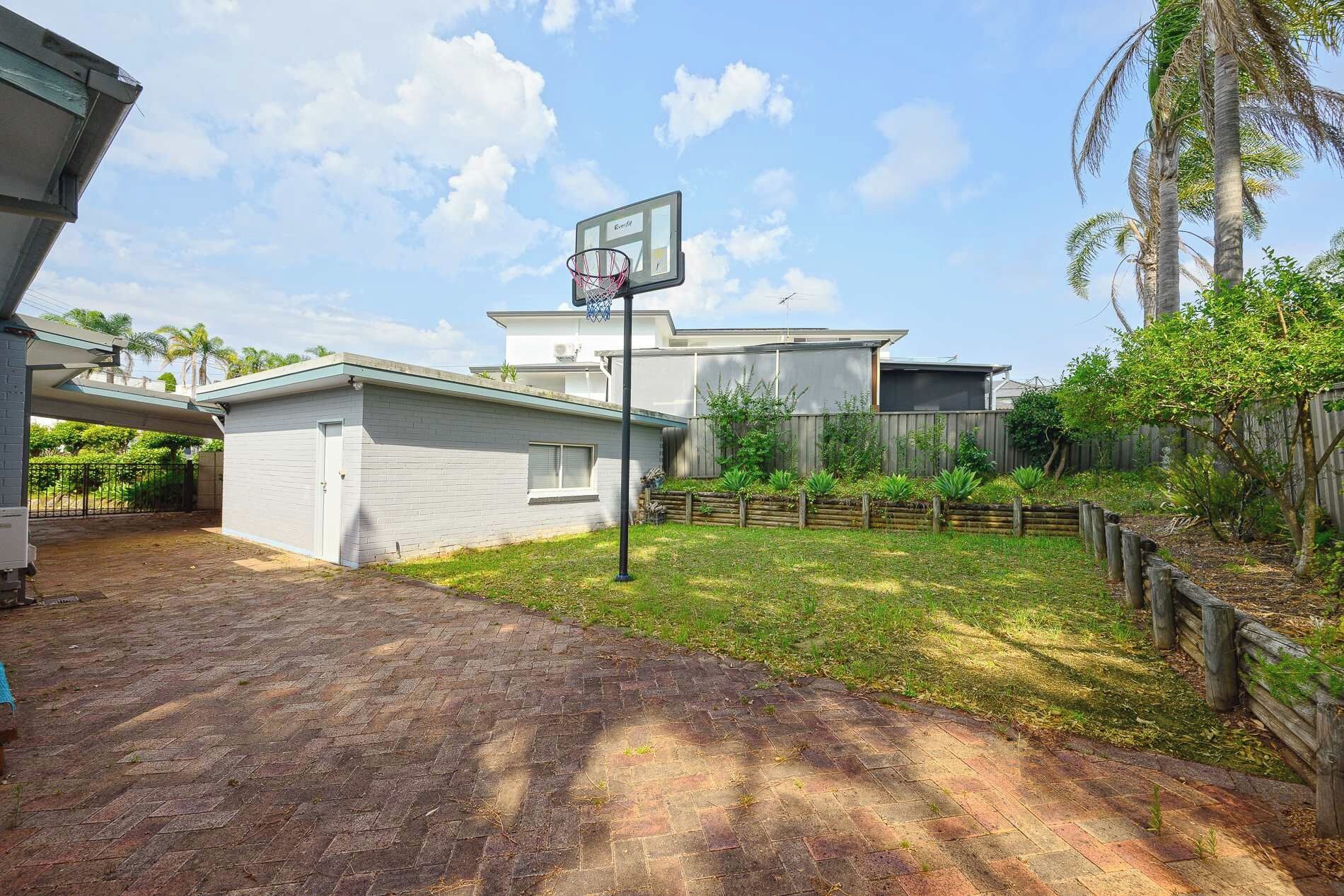 A residential backyard with a basketball hoop, a brick pathway, and a wooden fence.