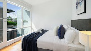 A bedroom with a bed, pillows, a lamp, and a view through a glass door. - 4BR Marsfield Stay  Walk to Macquarie Uni Metro (Marsfield)