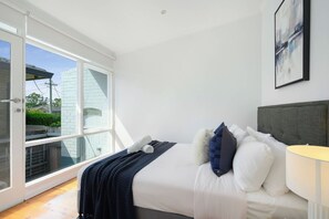 Een slaapkamer met een bed, kussens, een lamp en uitzicht door een glazen deur.