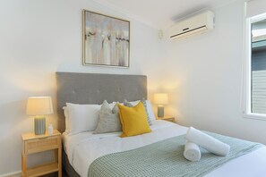 A hotel room with a bed, two bedside lamps, a wall-mounted air conditioner, and a window.