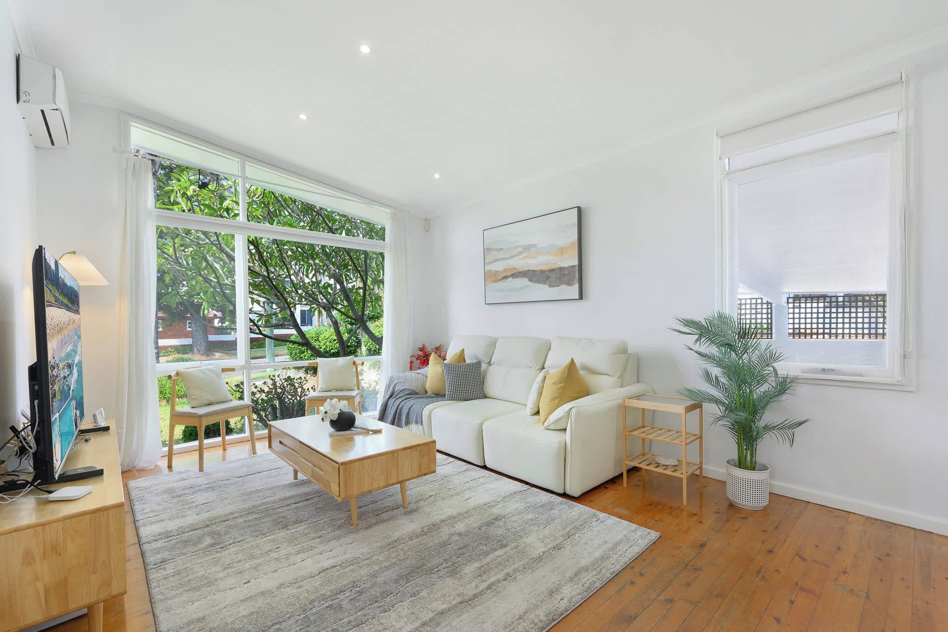 A modern living room with a sofa, coffee table, and a large window offering a view of greenery outside.