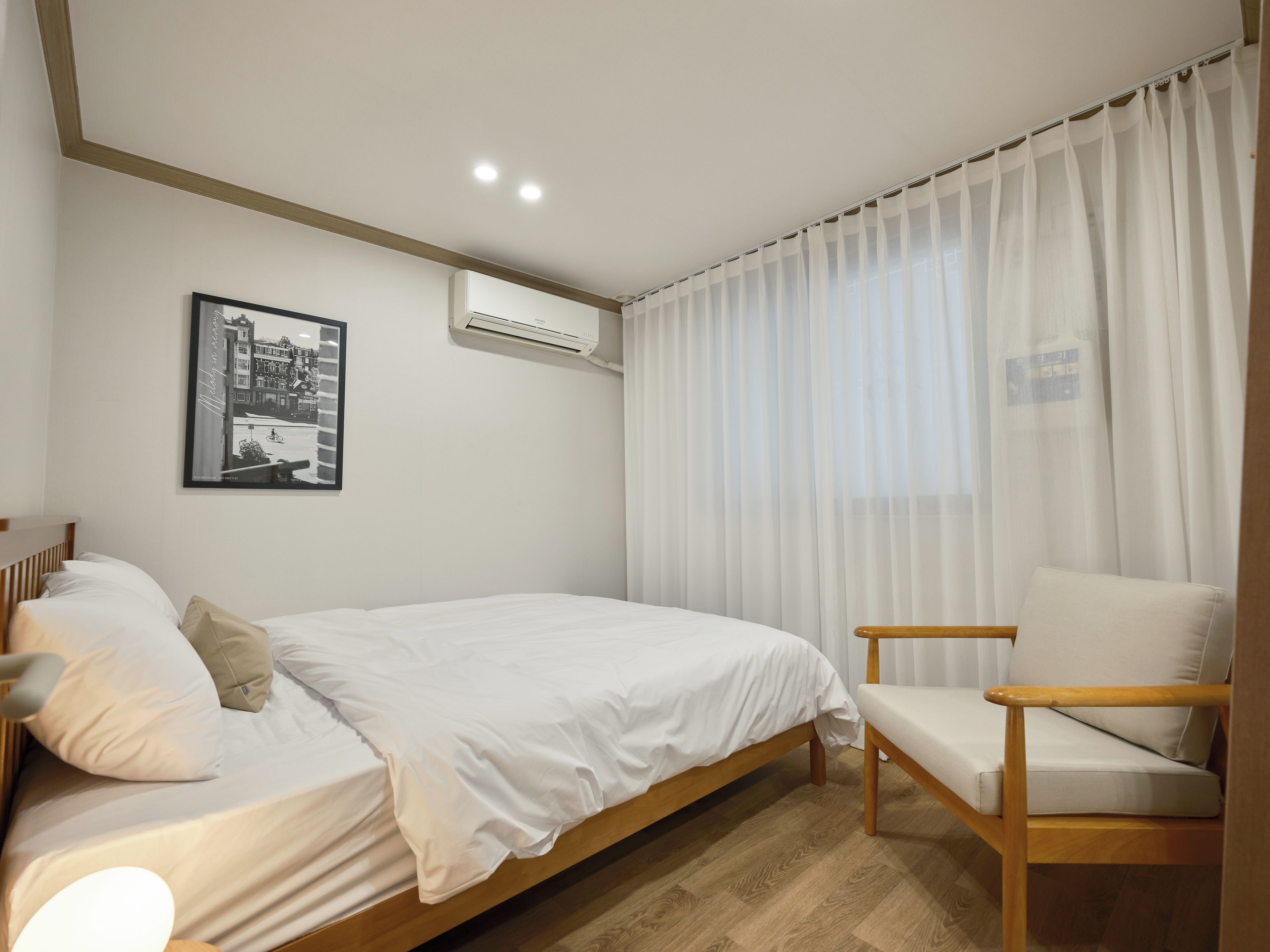 A bedroom with a bed, a chair, a wall-mounted air conditioner, and a framed picture.