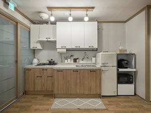 A compact kitchen with wooden cabinets, a built-in stove, a refrigerator, and a countertop with various kitchen items. - SunYou Stay (Andong)