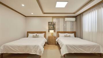A hotel room with two beds, a nightstand with a lamp, an air conditioning unit, and a window with curtains.