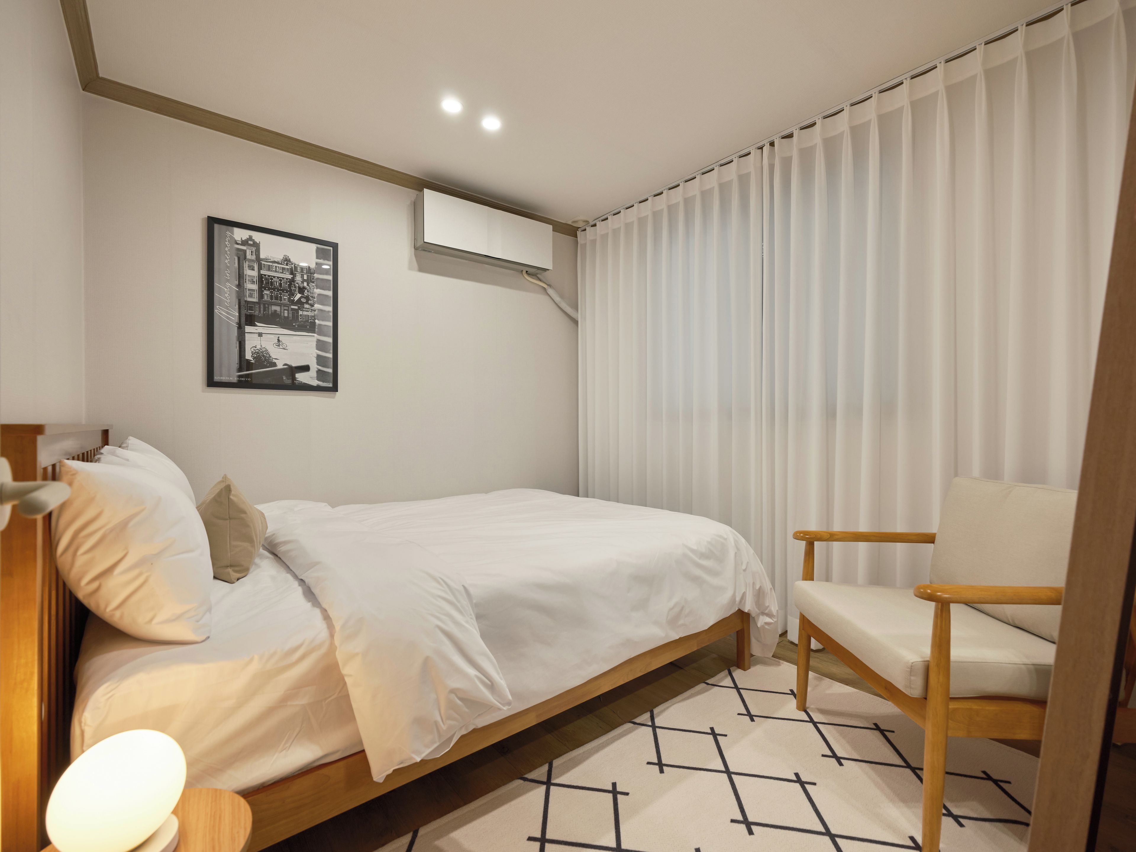A bedroom with a bed, a chair, a picture on the wall, and a window with curtains.