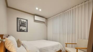 A bedroom with a bed, a chair, a picture on the wall, and a window with curtains.