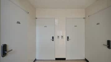 Een gang met twee deuren, waarop respectievelijk de aanduidingen 203 en 202 staan, elk met een moderne deurklink en een klein paneel aan de muur.