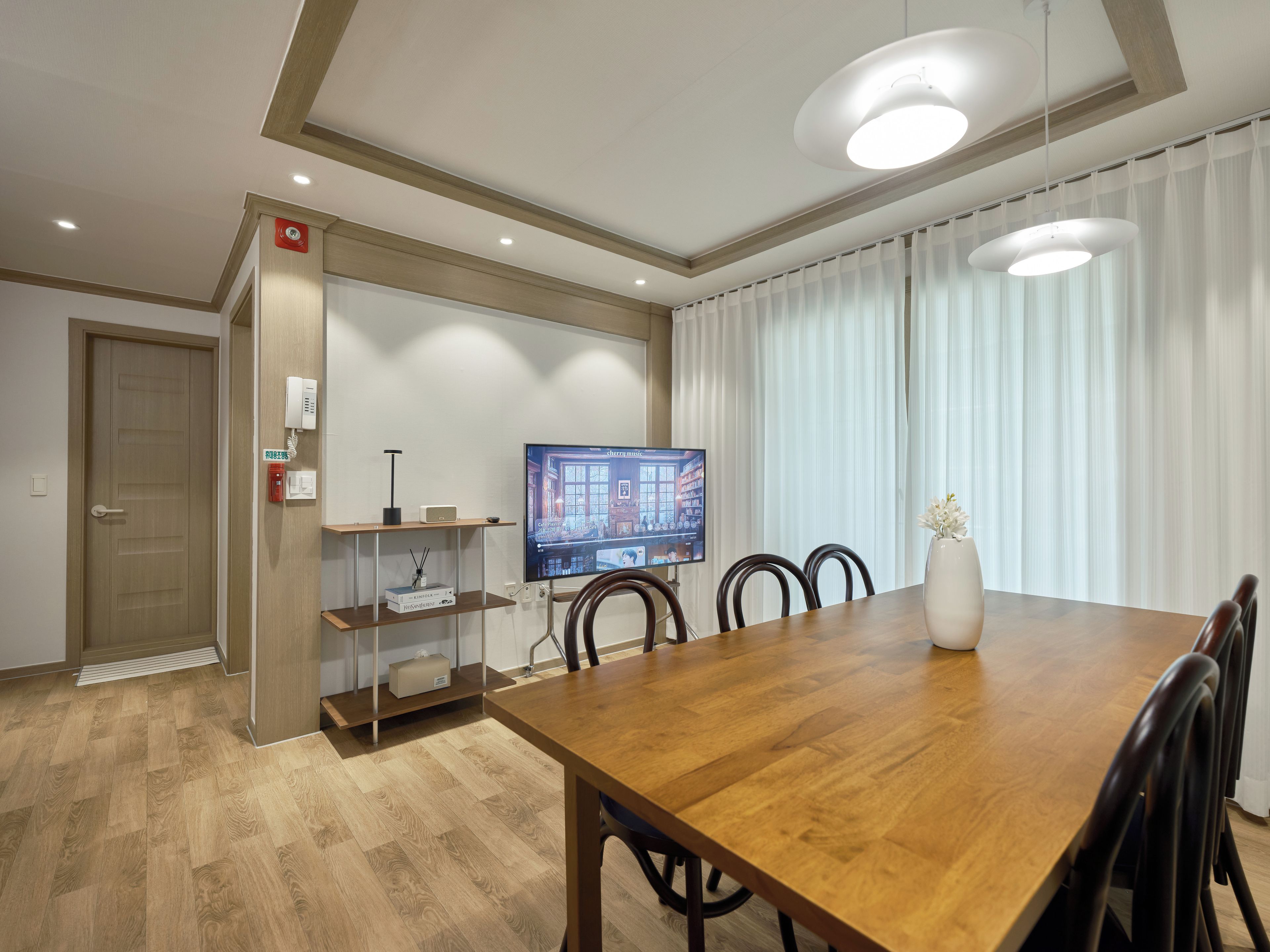 Un comedor moderno con una mesa de madera, sillas, un televisor y un jarrón con flores.