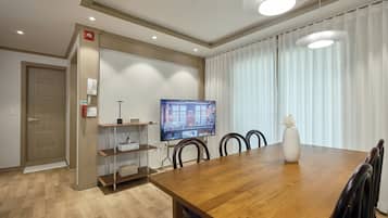 Un comedor moderno con una mesa de madera, sillas, un televisor y un jarrón con flores.