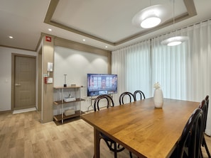 A modern dining area with a wooden table, chairs, a television, and a vase with flowers. - SunYou Stay (Andong)