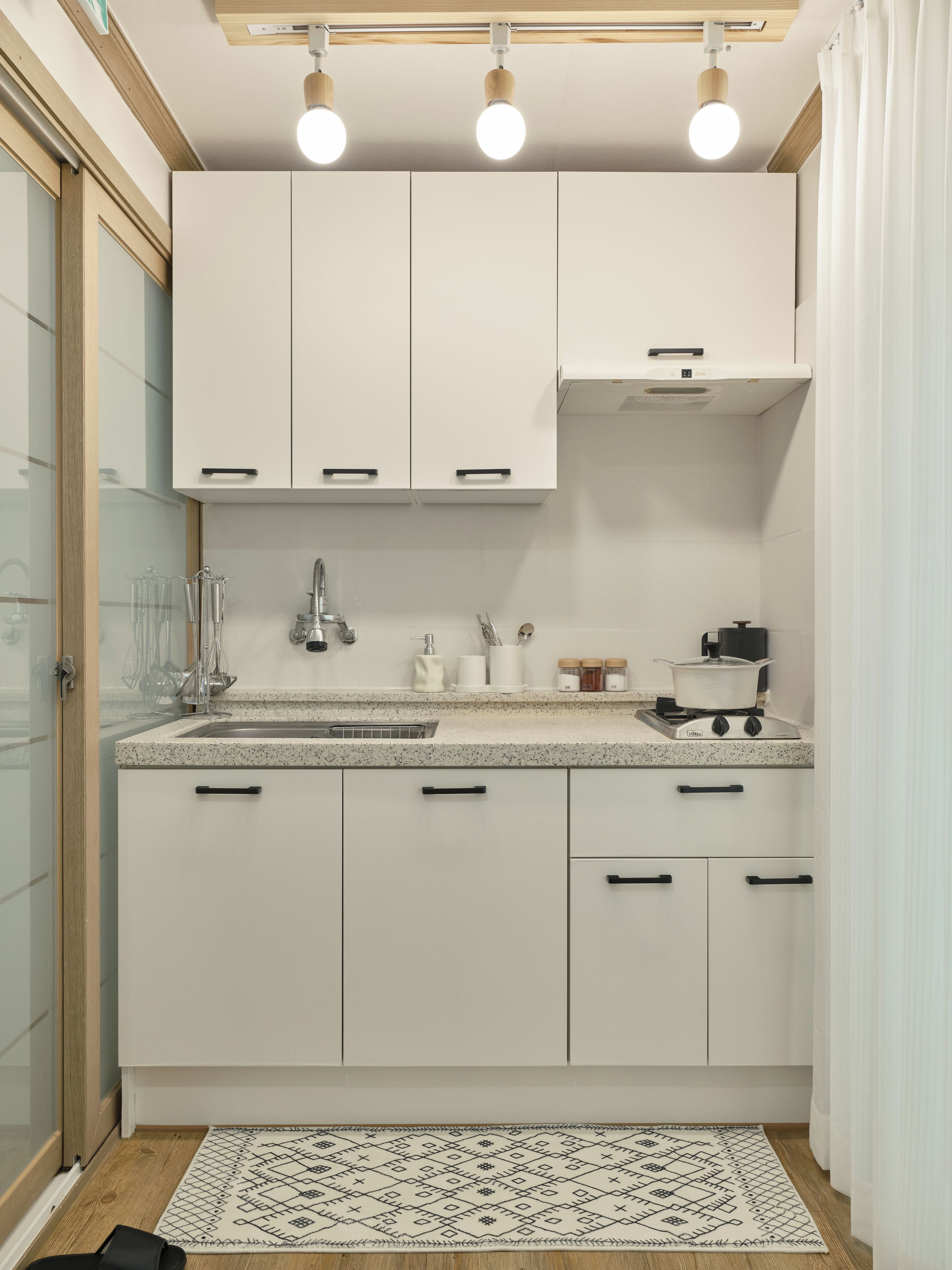 A modern kitchen with white cabinets, a granite countertop, a sink, a stove, and overhead lighting.