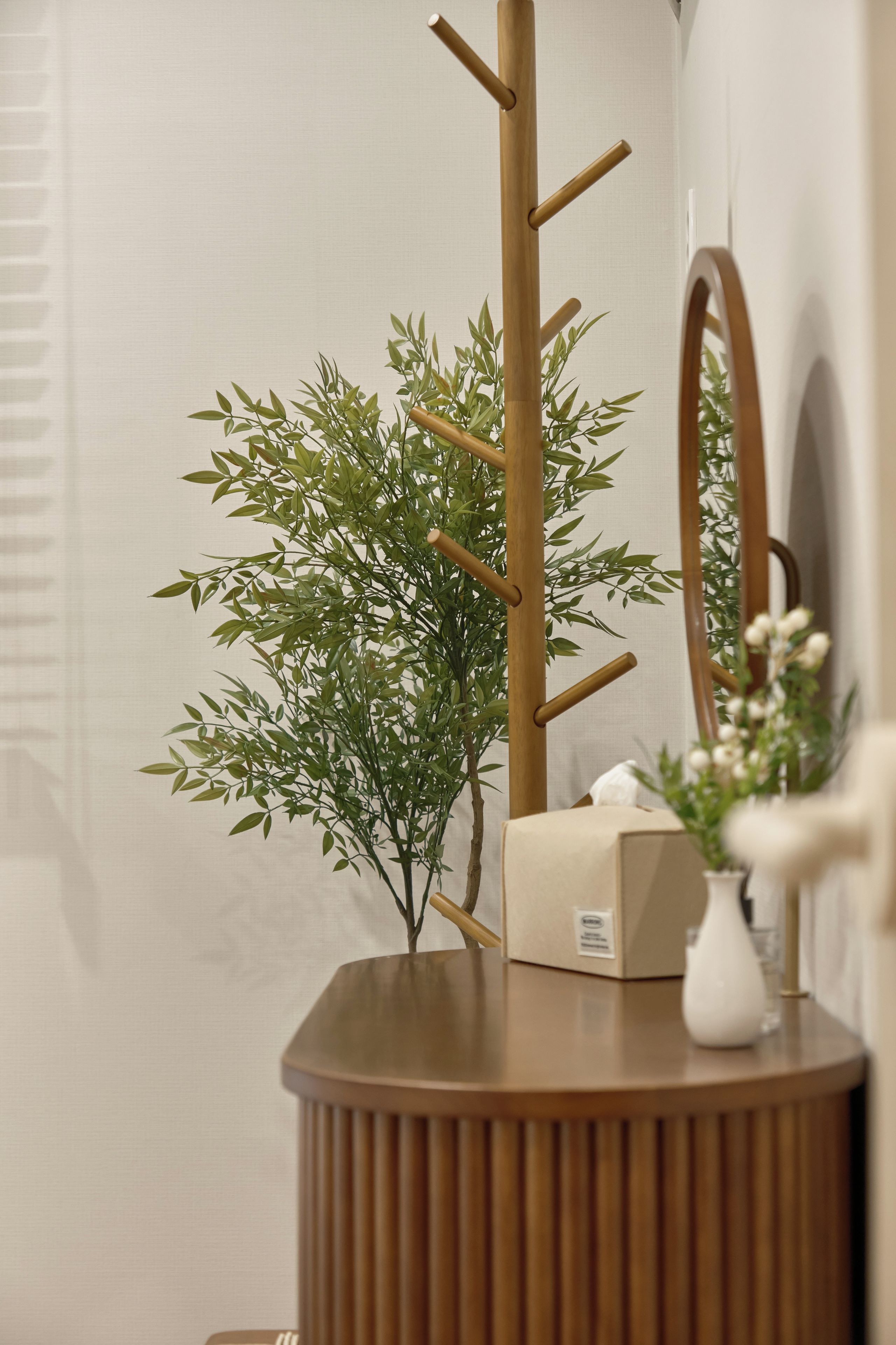 A wooden vanity with a mirror, a small plant, and a tissue box.