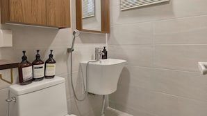 Ein Badezimmer mit Toilette, Waschbecken und Spiegel. Auf dem Spülkasten liegen drei Shampoo-Flaschen.