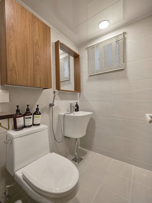 A bathroom with a toilet, sink, and mirror. There are three bottles of shampoo on the toilet tank. - SunYou Stay (Andong)