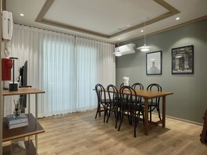 A dining area with a wooden table and chairs, a white vase with flowers, and two framed pictures on the wall.