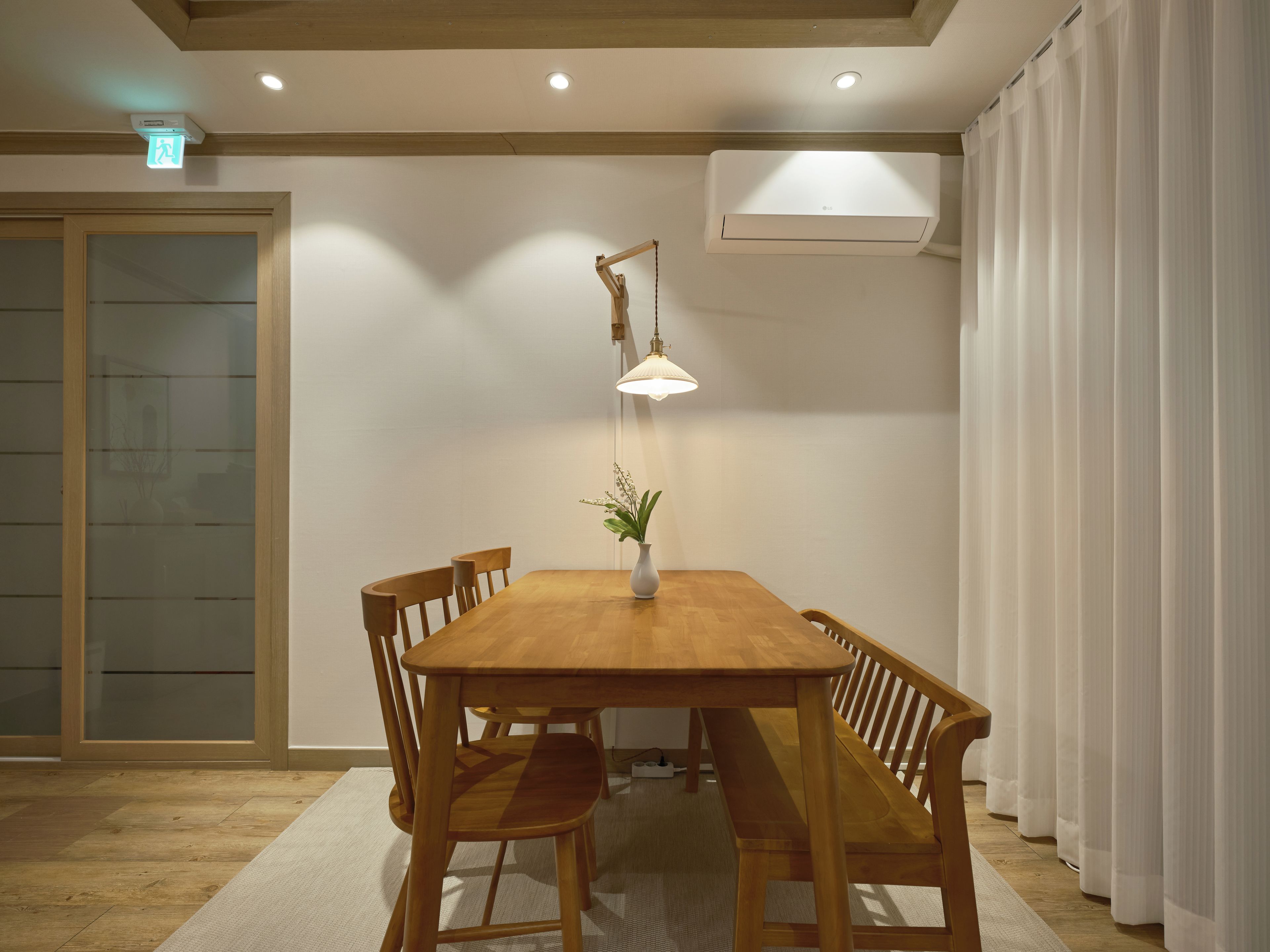 A dining area with a wooden table, chairs, a pendant light, and an air conditioning unit.
