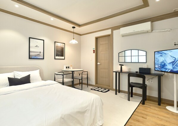 A hotel room with a bed, a desk with a chair, a television, and a small table with a chair.