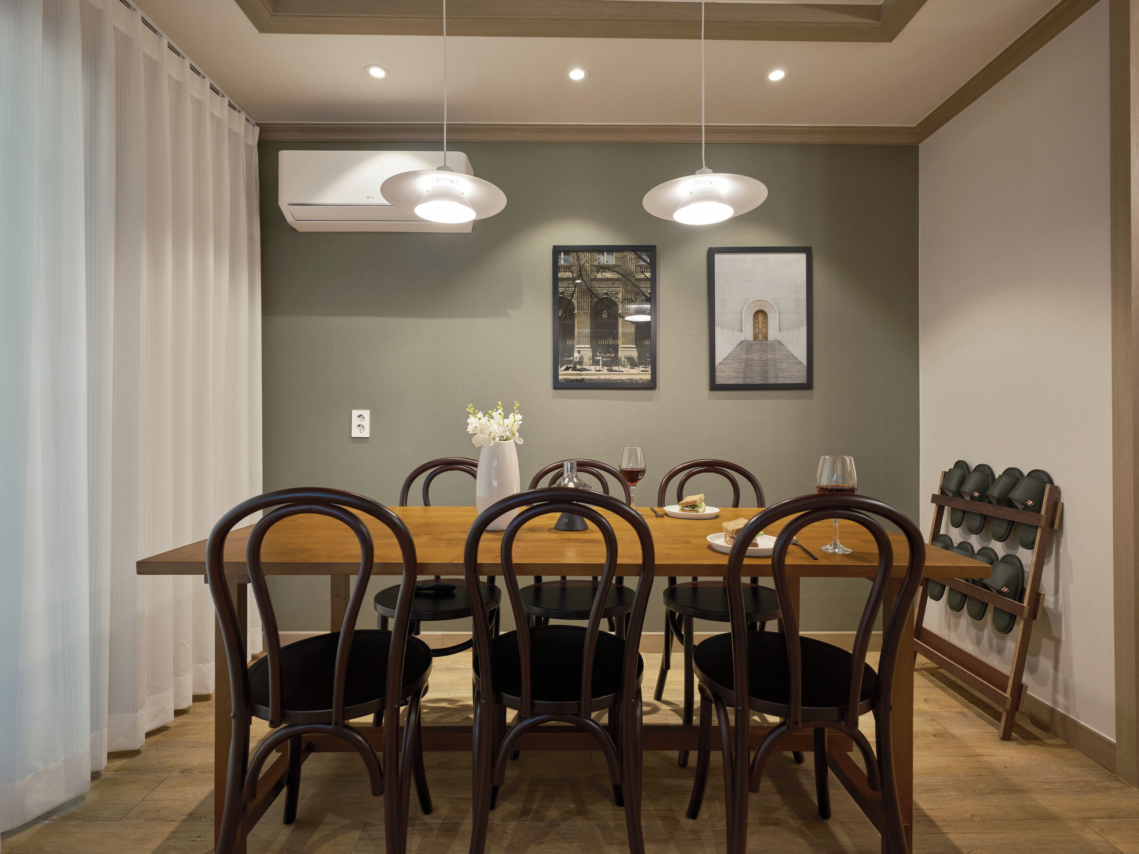 A dining area with a wooden table, six chairs, two pendant lights, and a wall-mounted shoe rack.