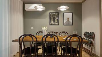 A dining area with a wooden table, six chairs, two pendant lights, and a wall-mounted shoe rack.