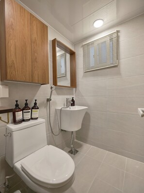 A bathroom with a toilet, sink, and mirror. There are three bottles of shampoo on the toilet tank.