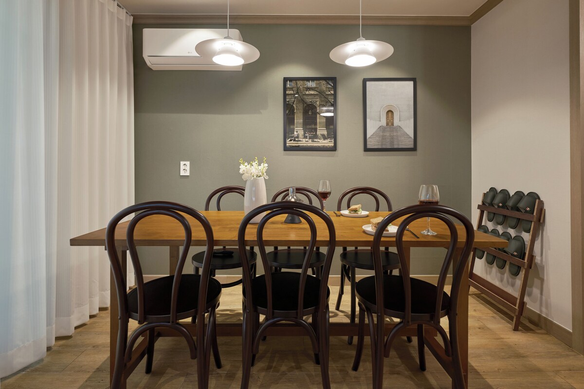 A dining area with a wooden table, six chairs, two pendant lights, and a wall-mounted shoe rack.