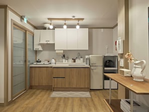 A modern kitchen with wooden cabinets, a built-in oven, a refrigerator, and a coffee machine. - SunYou Stay (Andong)
