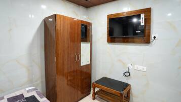 Quarto com guarda-roupa de madeira, um pequeno banco de madeira, televisão fixada na parede e cama com colcha estampada.