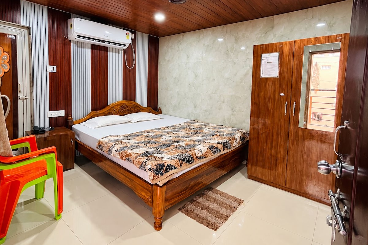 A hotel room with a wooden bed, a wardrobe, a desk, a chair, and an air conditioning unit.